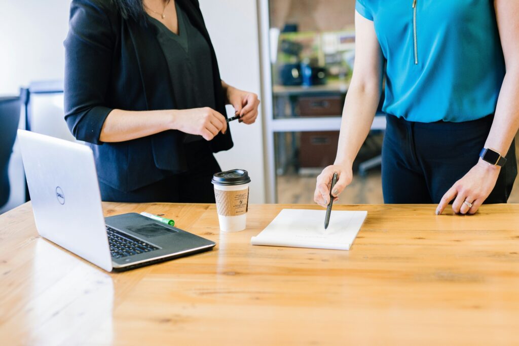 Two women infront of a desk with a laptop and document on it