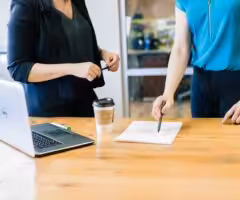 Two women infront of a desk with a laptop and document on it