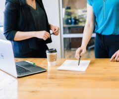 Two women infront of a desk with a laptop and document on it