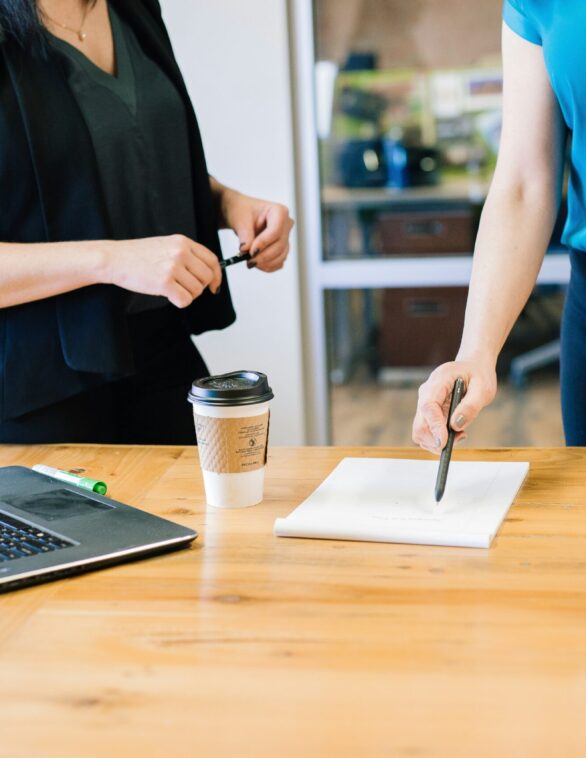Two women infront of a desk with a laptop and document on it